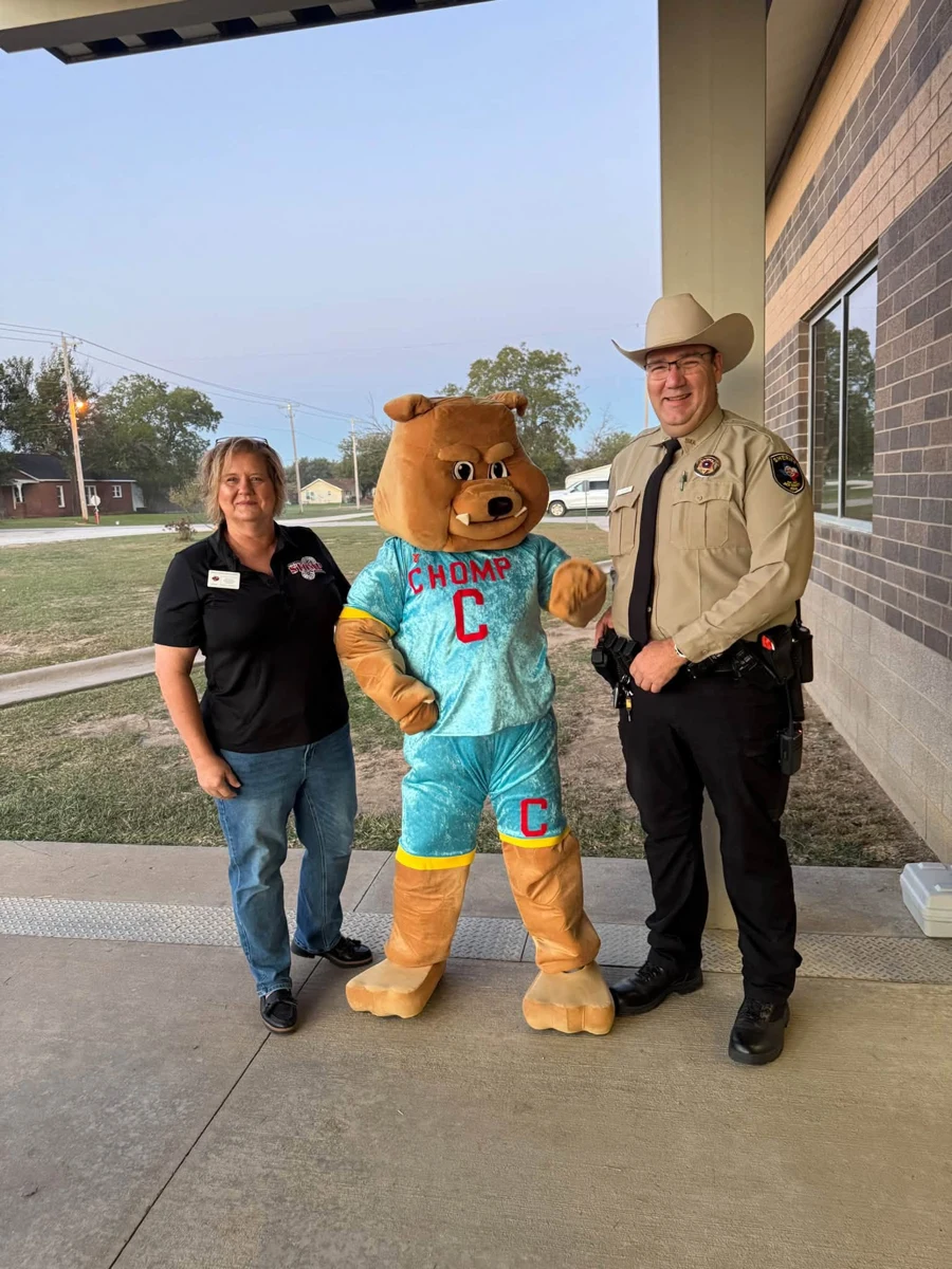 CHOMP mascot posing with two adults outside Bryson Elementary