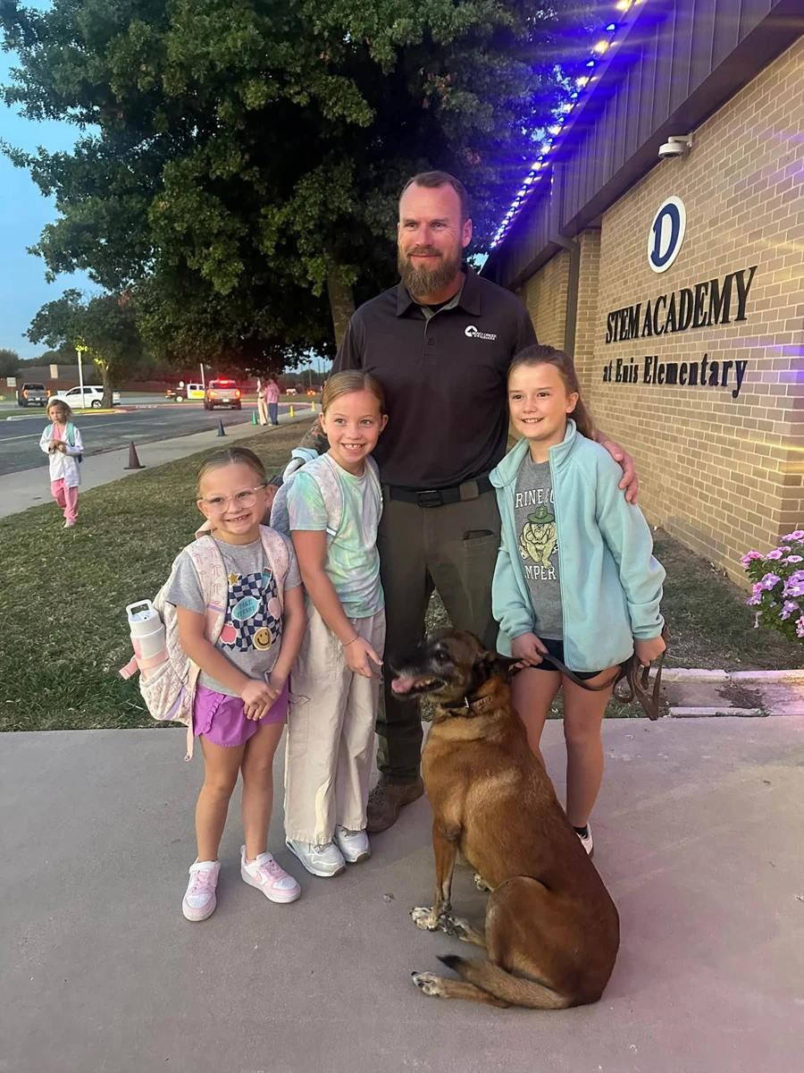 An officer and dog posing with three students