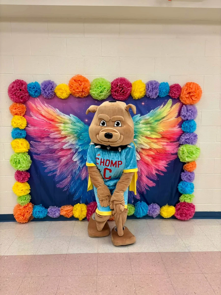 CHOMP mascot posing in front of a colorful wing backdrop at Rann Elementary