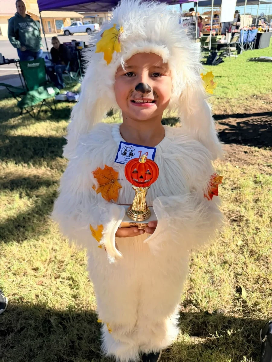 A child in a white furry costume holding a pumpkin trophy at STOMP Fest 2026